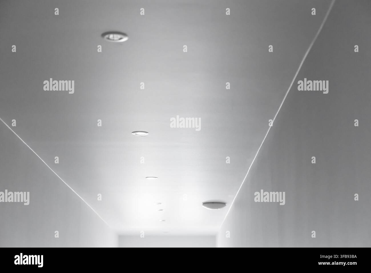 Una prospettiva minimalista di un soffitto di corridoio contemporaneo e luminoso con una serie di punti luce incassati e linee architettoniche diagonali sottili Foto Stock