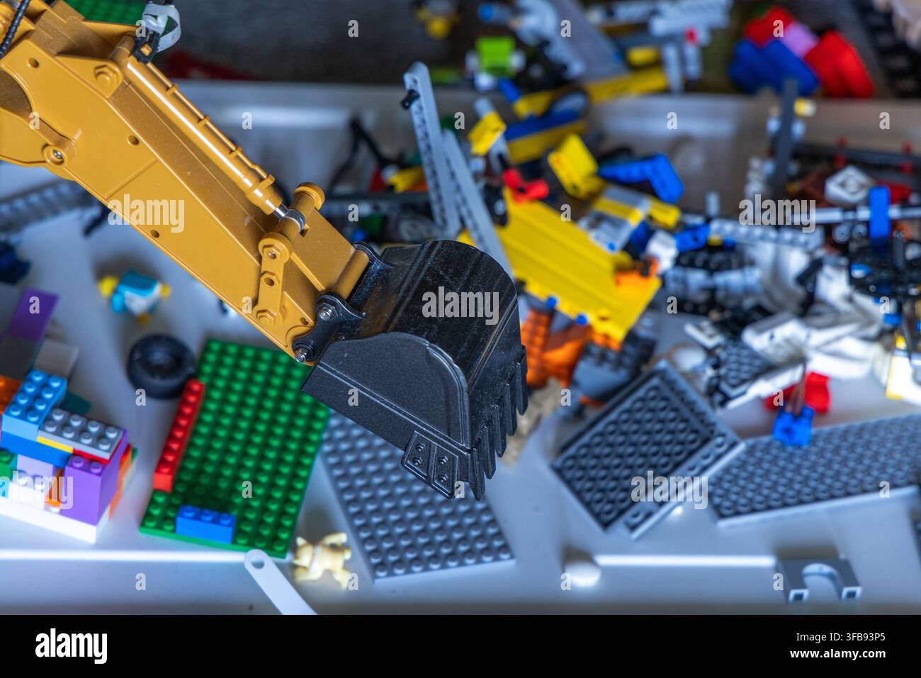 Un braccio e una benna di un escavatore giocattolo giallo sono posizionati sopra una raccolta sparsa di blocchi da costruzione colorati e pezzi di giocattoli di costruzione Foto Stock