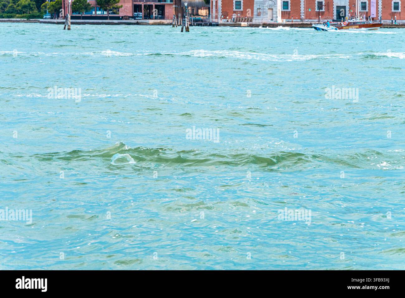 Acqua blu agitata riempie lo sfondo con edifici sul lungomare e piccole barche in lontananza. Foto Stock