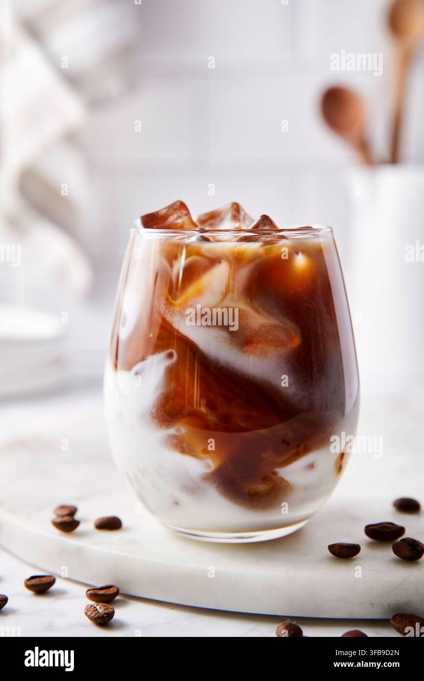 Caffè Latte ghiacciato. Caffè scuro mescolato con latte e cubetti di ghiaccio. Illuminazione luminosa in cucina. Foto Stock