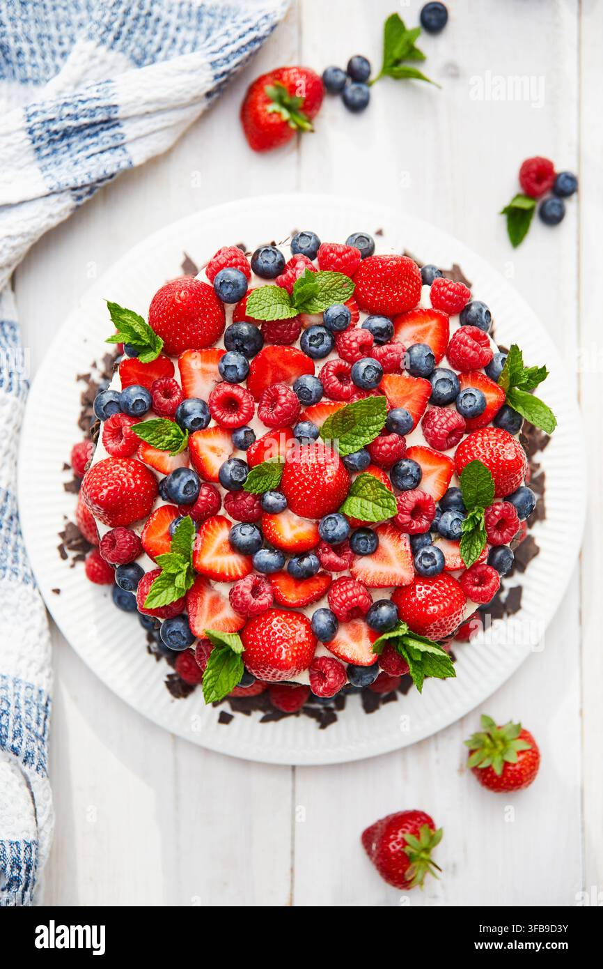 Torta di fragole con mirtilli, lamponi e foglie di menta. Illuminazione soleggiata, fresca, estiva. Prospettiva flat-lay. Foto Stock