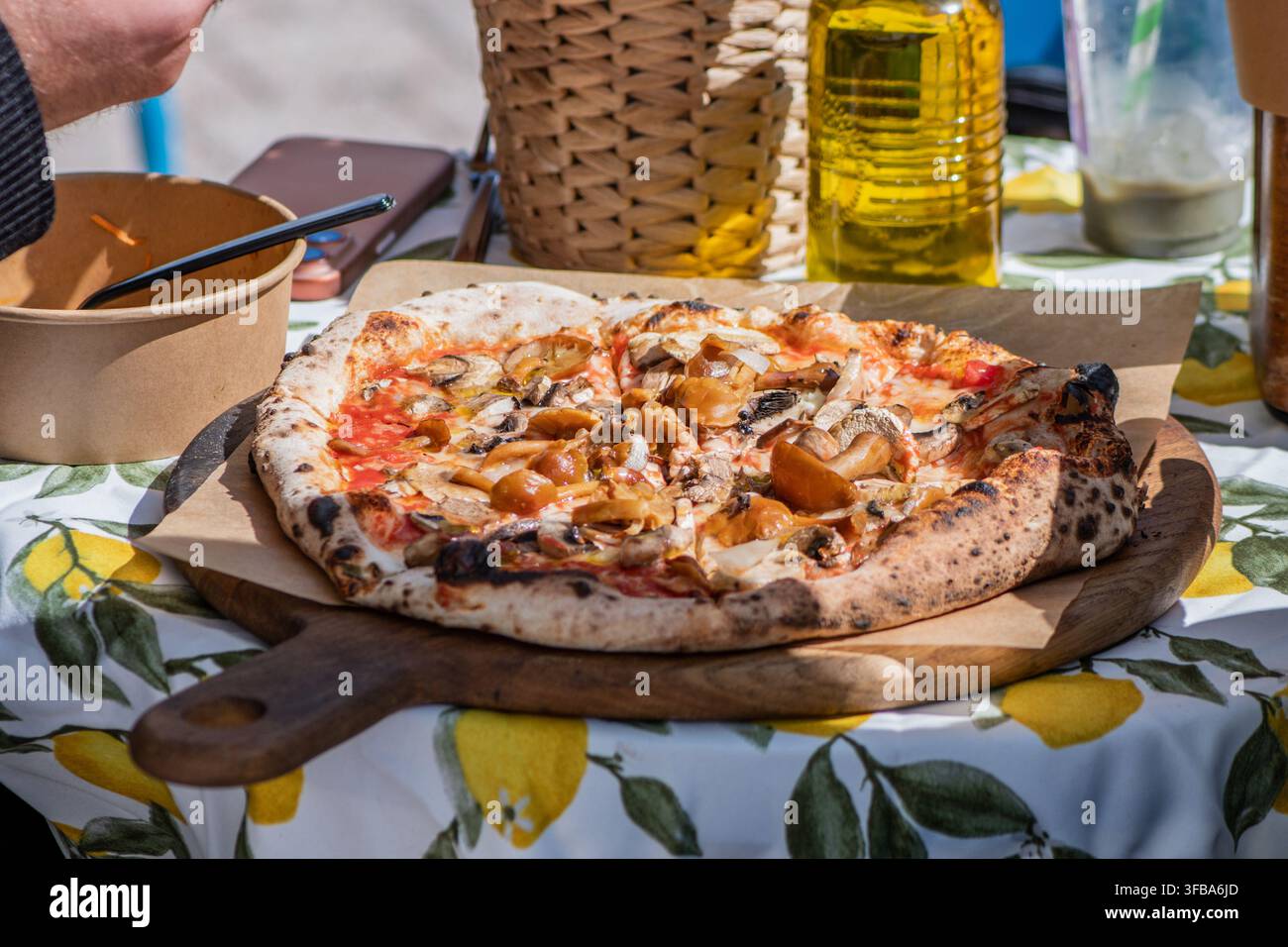 Pizza cotta nel forno a legna in stile napoletano appena sfornata con funghi selvatici, servita su una tavola di legno sopra una tovaglia a motivi di limone Foto Stock