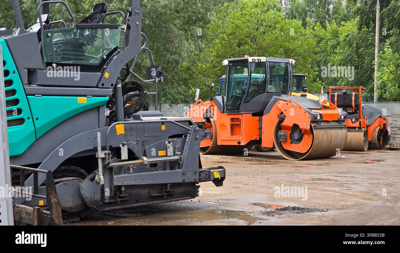 Macchinari pesanti e piallatrici asfaltiche industriali sono parcheggiate all'aperto in un cantiere per lo sviluppo stradale. Foto Stock