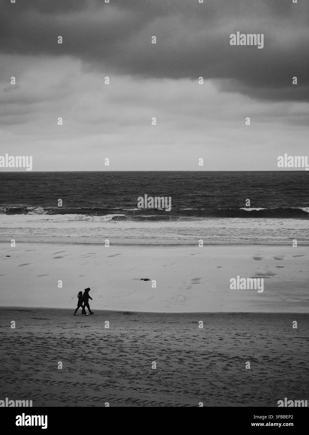 Immagine in bianco e nero di una persona che cammina sulla riva di una spiaggia in Cantabria, Spagna Foto Stock