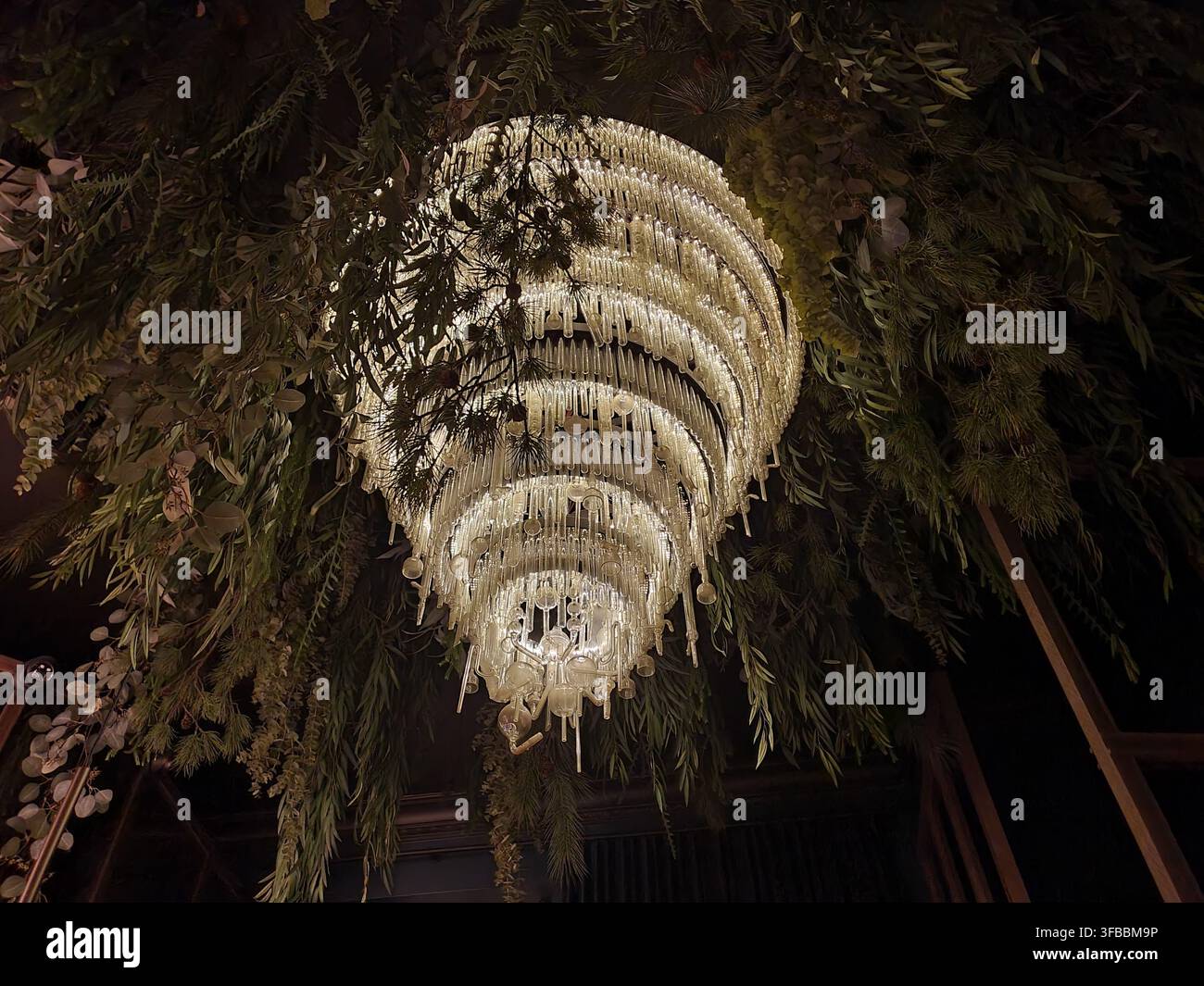 Un impressionante lampadario a spirale di cristallo pende dal soffitto, circondato da abbondante vegetazione a cascata e installazioni botaniche. Il multi-livello Foto Stock