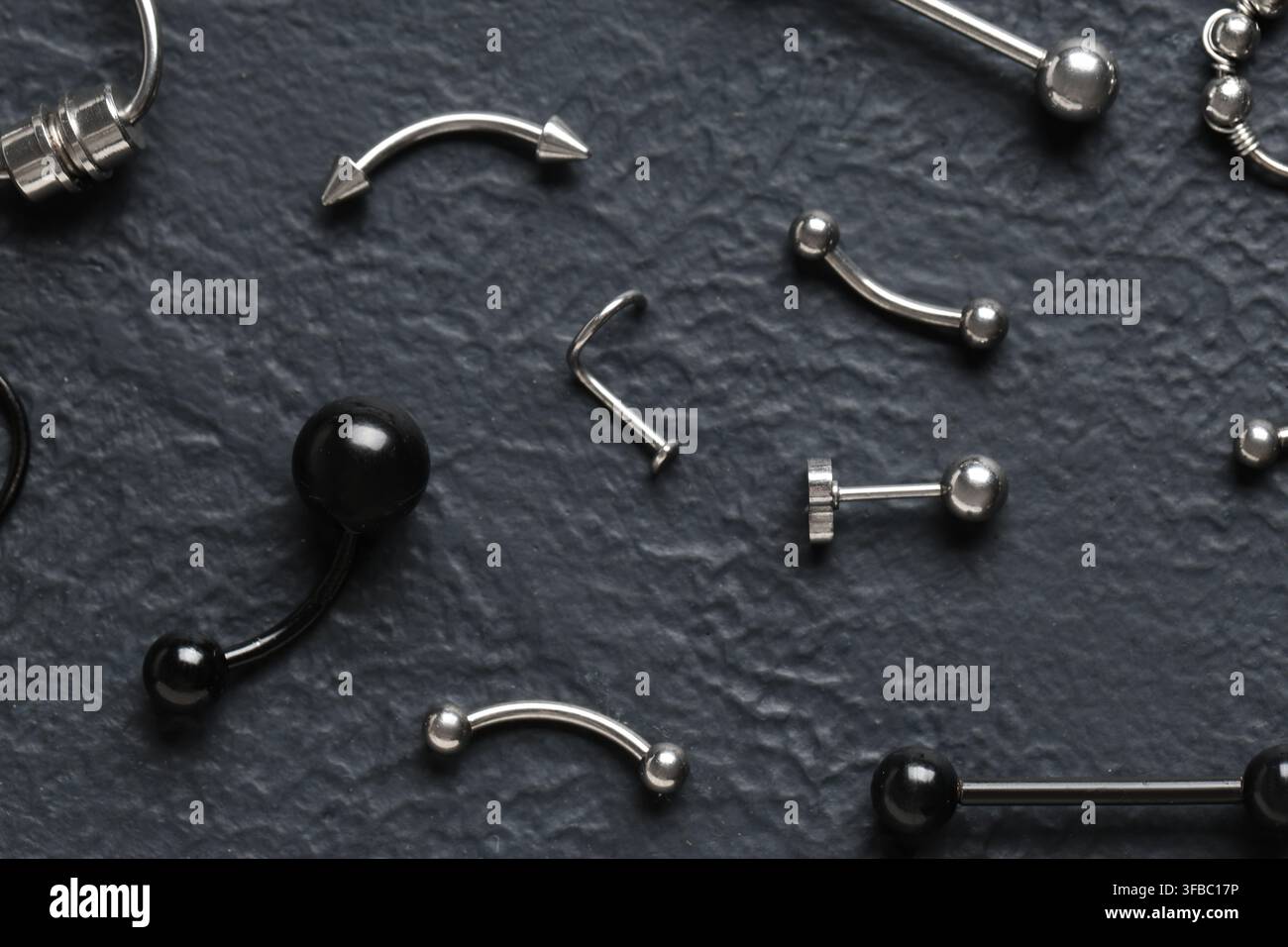 Collezione di gioielli per piercing corporei, moda alternativa e autoespressione, vari borchie in metallo e nero, anelli e bilancieri su sfondo scuro Foto Stock