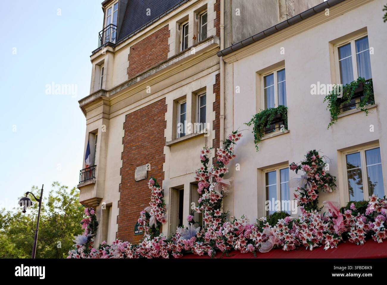 Decorazioni floreali rosa e bianche coprono la facciata di un edificio con finestre e una bandiera francese a Montmartre, Parigi, Francia. Foto Stock
