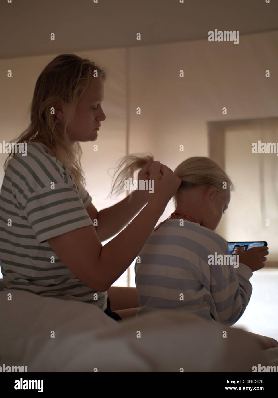 Donna si lega una coda di cavallo mentre una ragazza guarda lo schermo del telefono Foto Stock