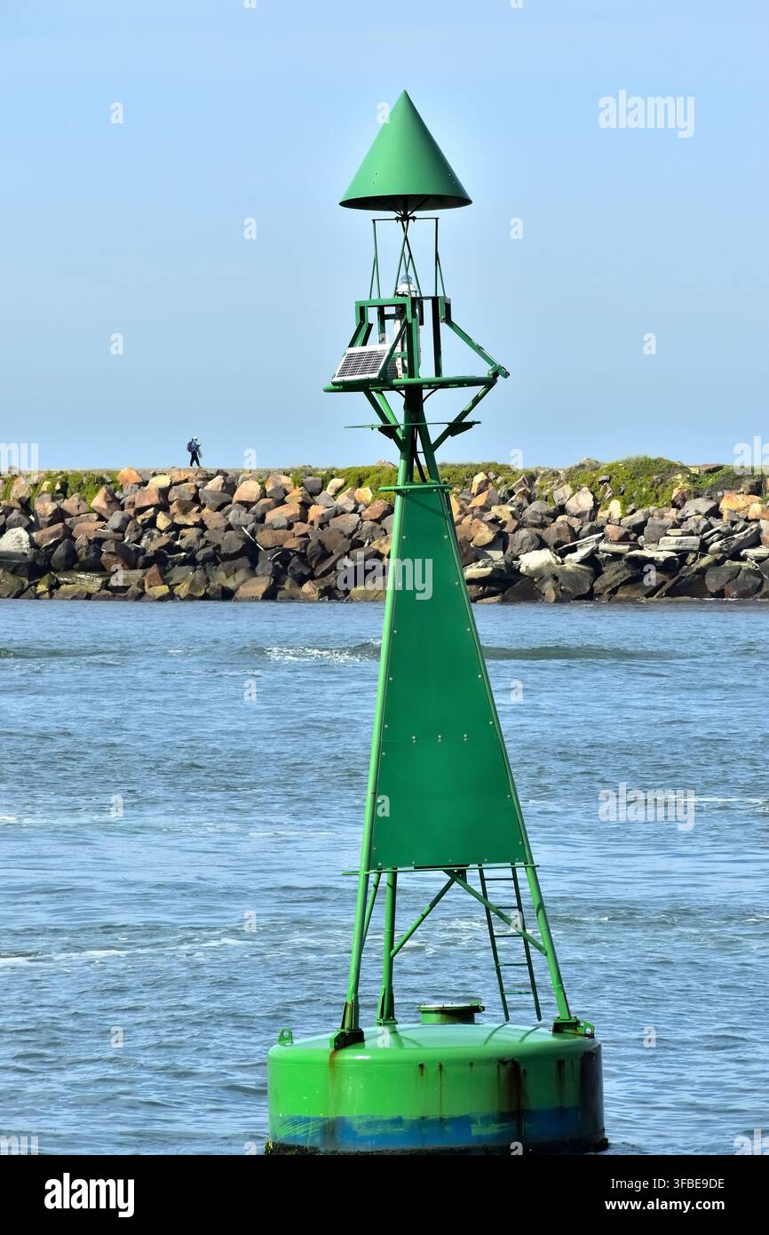 Una boa di navigazione verde e alta galleggia su acque costiere calme, dotata di un marcatore conico e di apparecchiature a energia solare. Foto Stock