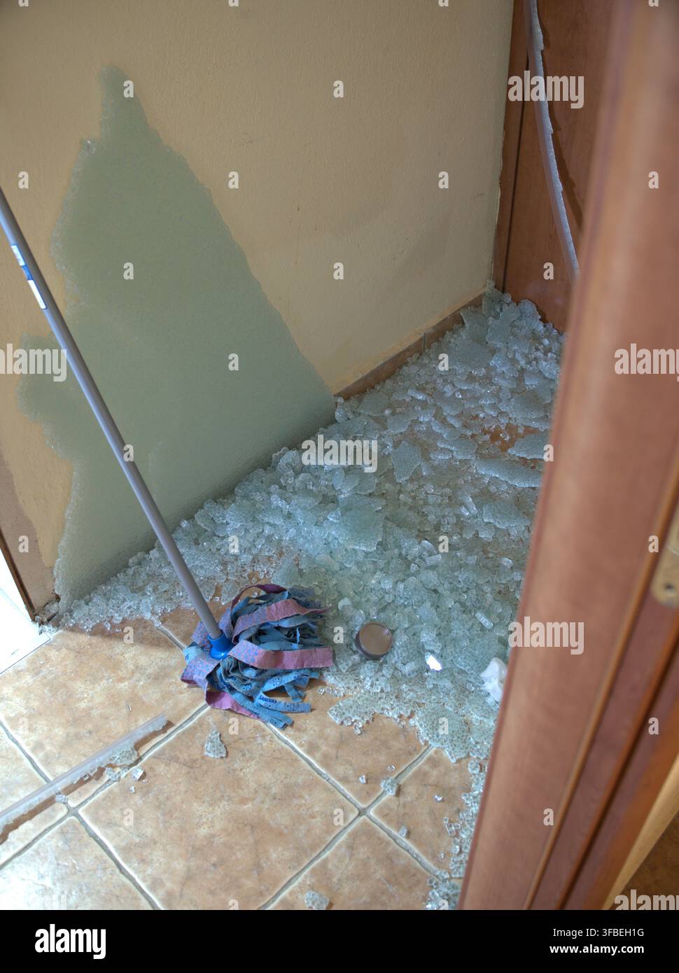 Vetro rotto sparso sul pavimento vicino alla porta con una scopa all'interno della casa Foto Stock