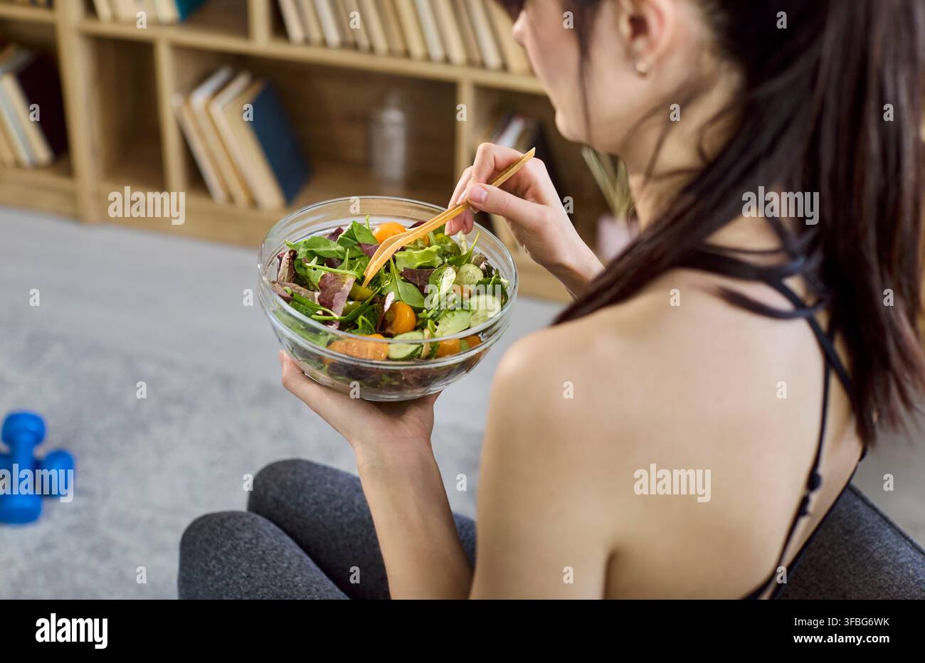 Donna in forma che mangia insalata fresca dopo l'allenamento a casa, concetto di dieta e nutrizione sana Foto Stock