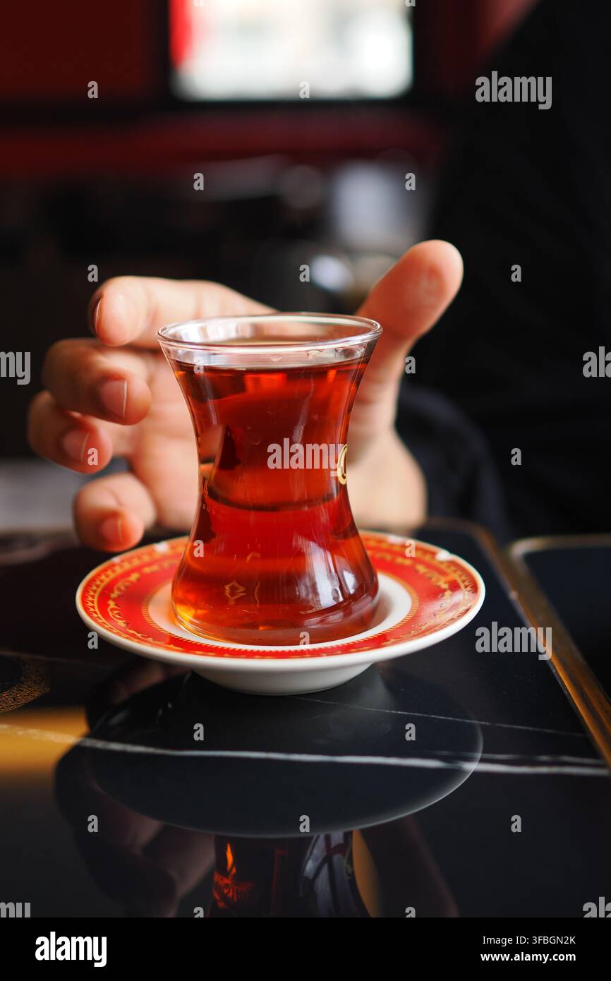 Mano che tiene una tazza di tè turco su un tavolo Foto Stock