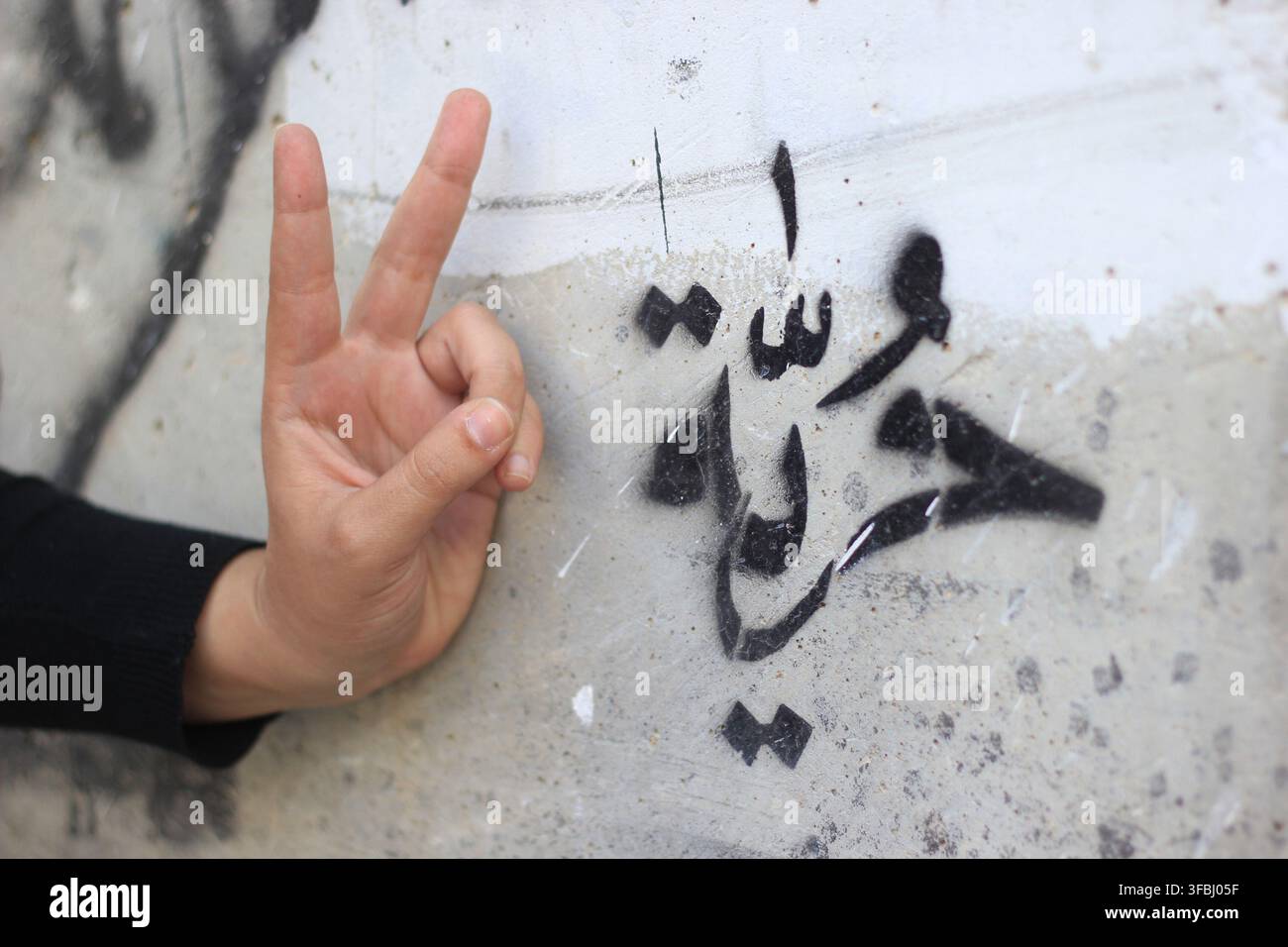Mano che fa un segno di vittoria accanto a graffiti arabi sul muro di separazione a Betlemme Foto Stock