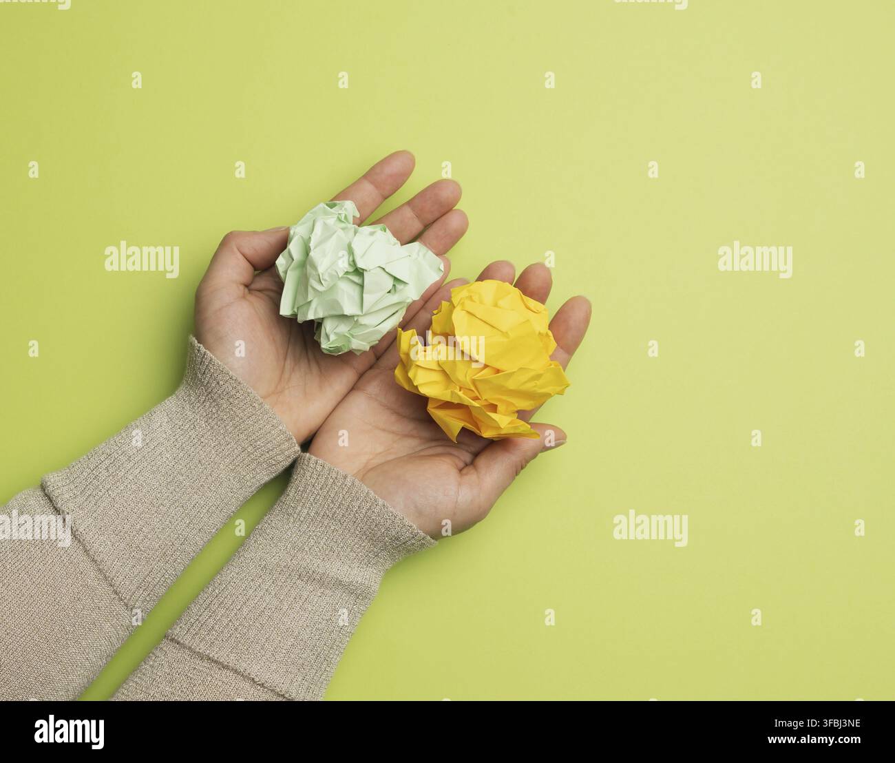 le mani femminili tengono un foglio di carta verde e giallo sbriciolato su uno sfondo verde, vista dall'alto Foto Stock