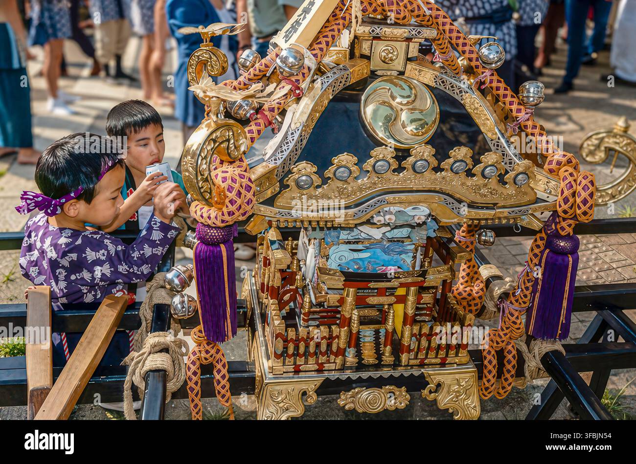 Bambini giapponesi accanto a un santuario portatile riccamente decorato durante un festival tradizionale Matsuri a Tokyo, in Giappone, che celebra la cultura locale. Foto Stock