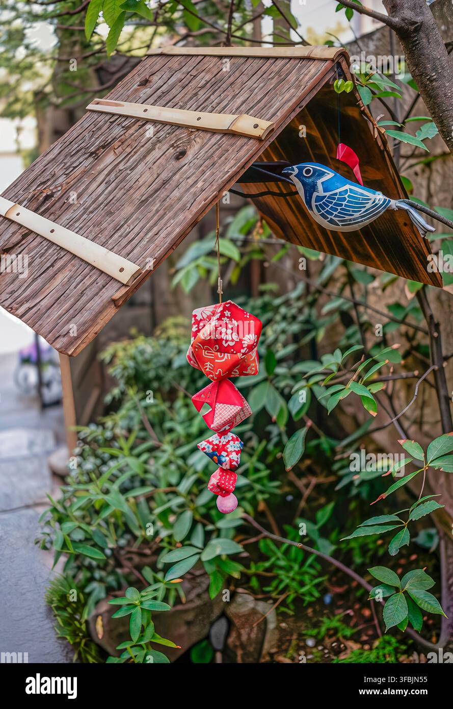 Decorazione tradizionale di negozio giapponese a Kamakura, Giappone, con un ornamento a forma di uccello in legno e ciondoli di stoffa colorati tra una vegetazione lussureggiante Foto Stock