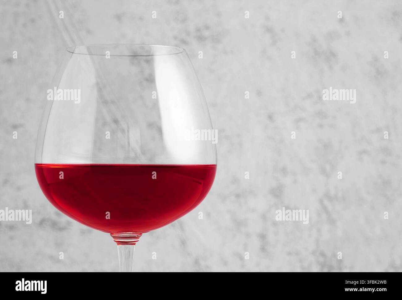 Vino rosso che riempie un grande bicchiere, presentando un concetto di bevanda minimalista ed elegante su uno sfondo grigio testurizzato Foto Stock