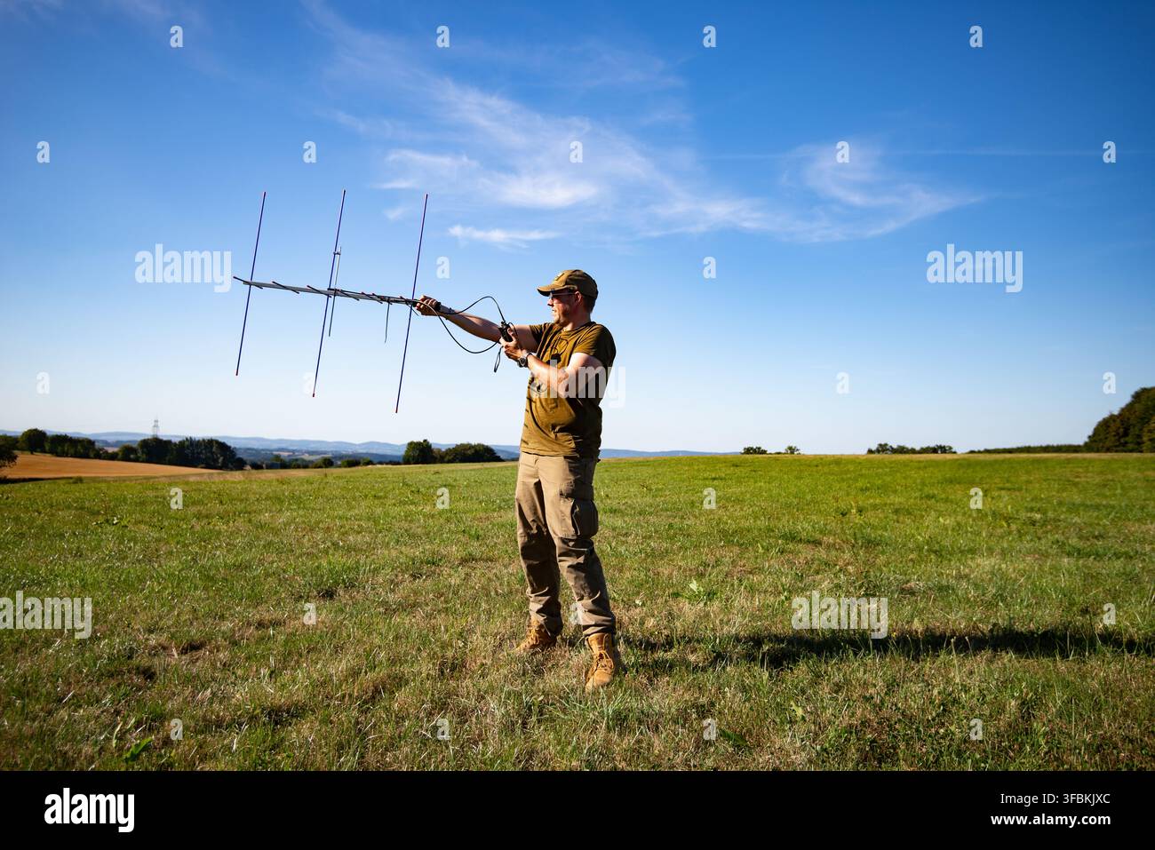 Operatore radioamatore che utilizza un'antenna direzionale Yagi in un campo aperto per la comunicazione satellitare e il rilevamento radio Foto Stock