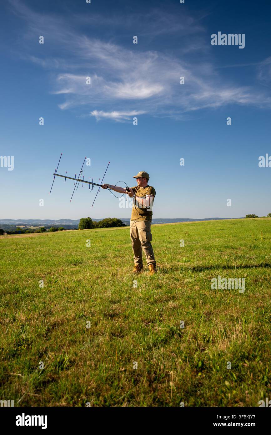 Operatore radioamatore che utilizza un'antenna direzionale Yagi in un campo aperto per la comunicazione satellitare e il rilevamento radio Foto Stock