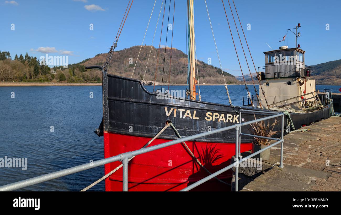 La storica barca a vapore Clyde Vital Spark è ormeggiata lungo il molo di Inveraray in una giornata serena, sullo sfondo delle acque scenografiche del Loch Fyne. Foto Stock