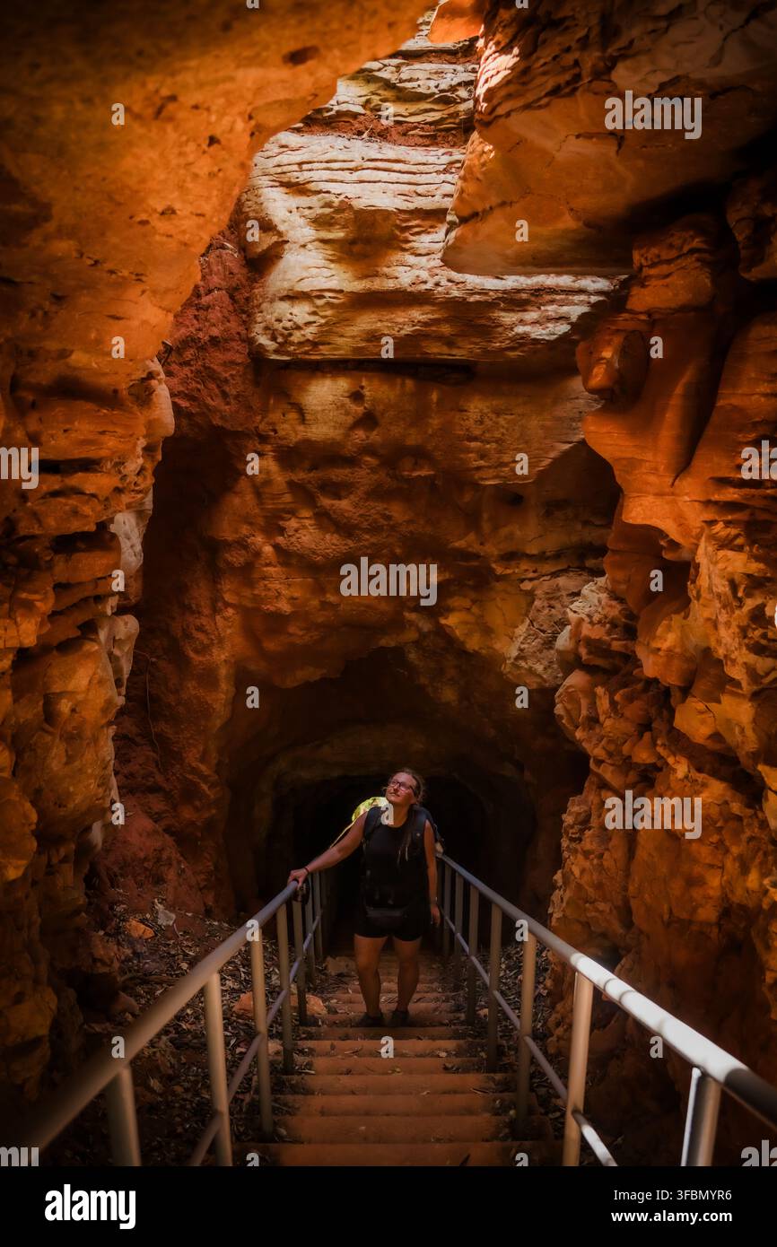Vista di un escursionista che scende una scala nella grotta del Monte Francese con pareti rocciose rosse e frastagliate e luce naturale che filtra dall'alto ad Antsiranana Foto Stock