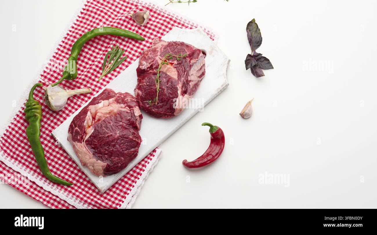 Pezzo grezzo di ribeye di manzo con rosmarino, timo su un tavolo bianco, vista dall'alto Foto Stock