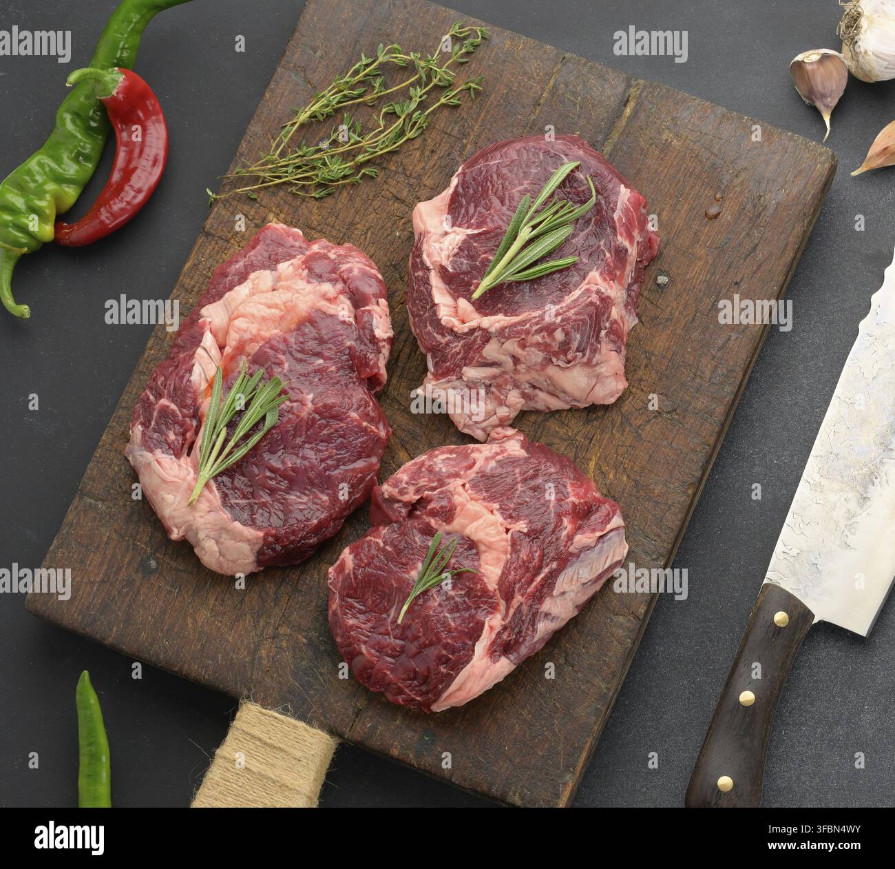 Pezzo grezzo di ribeye di manzo con rosmarino, timo su un tavolo nero, vista dall'alto Foto Stock