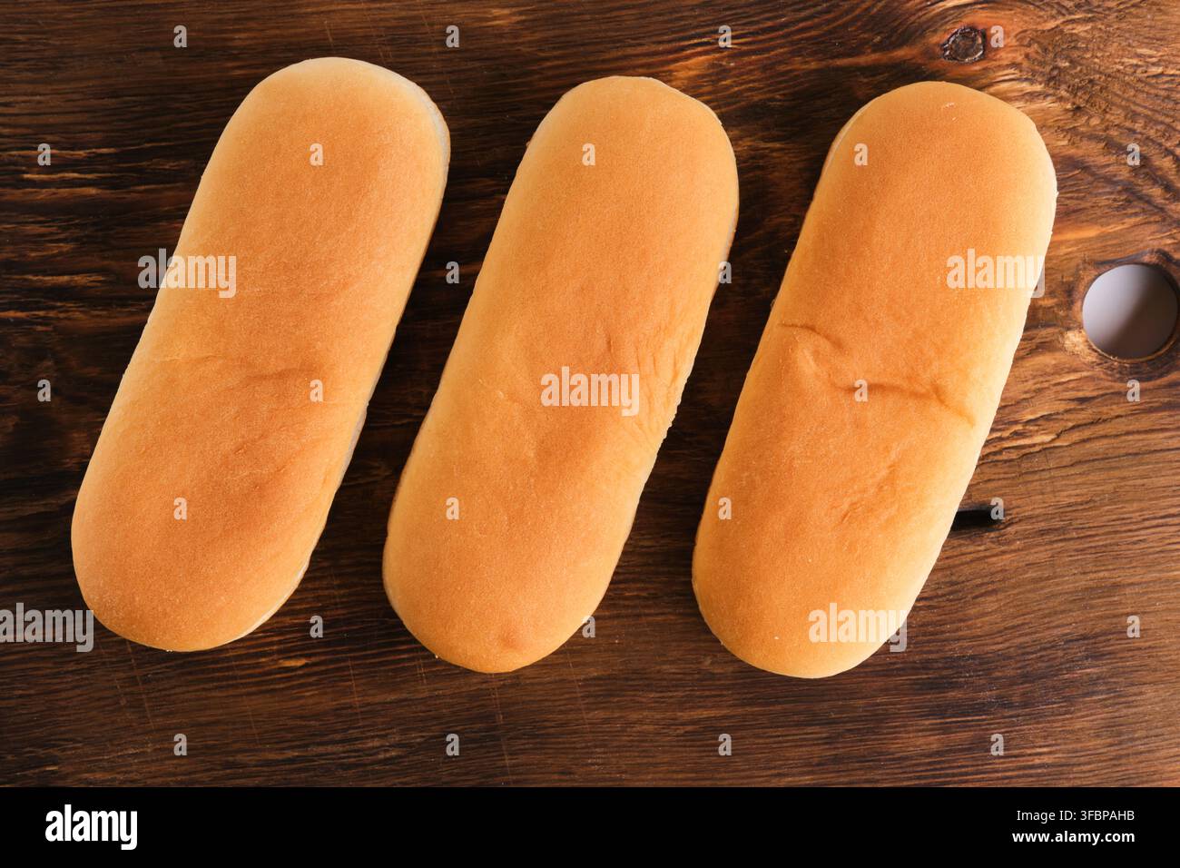 Vista dall'alto tre morbidi panini per hot dog disposti ordinatamente su uno sfondo di tagliere in legno vintage scuro Foto Stock