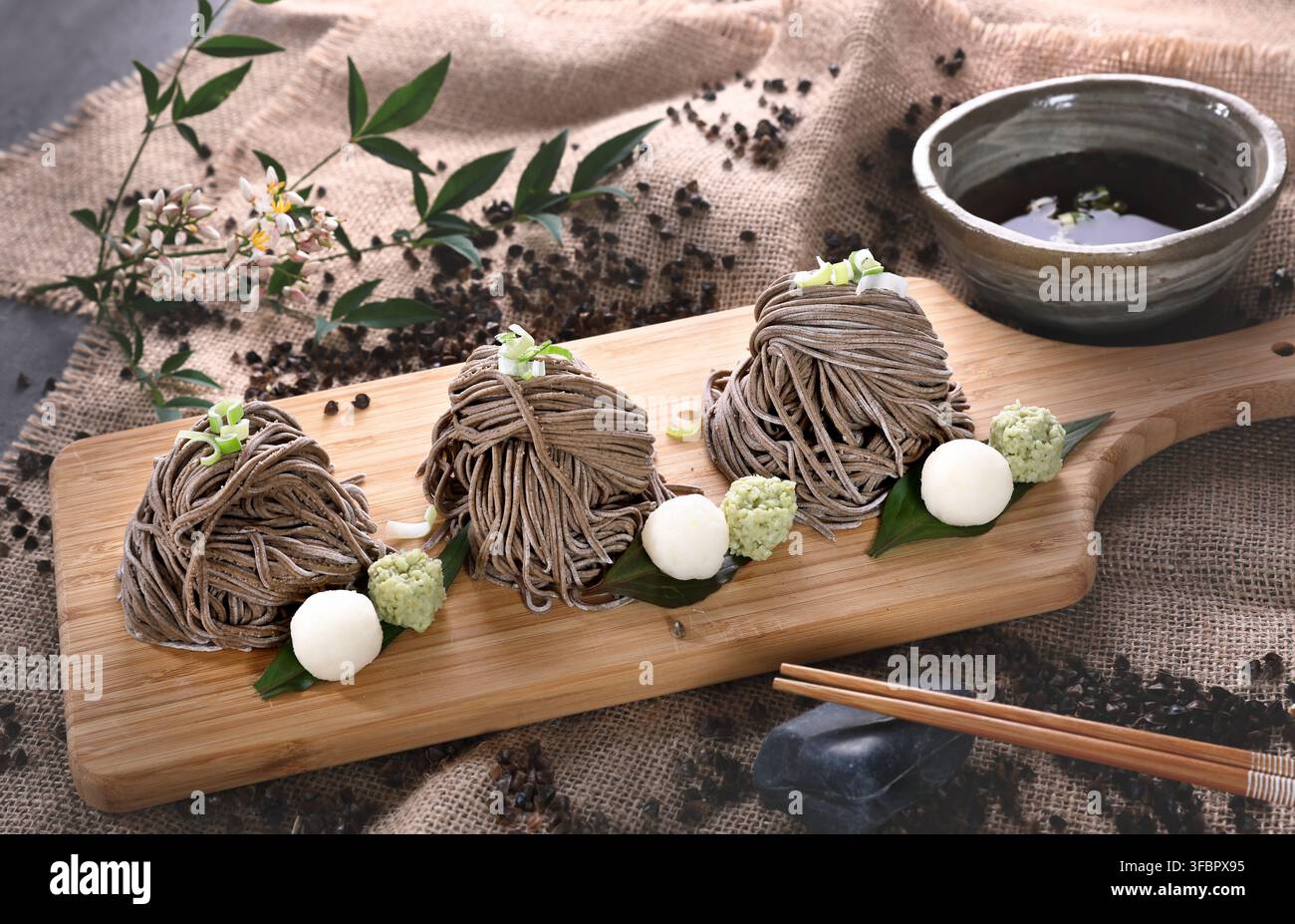 Presentazione elegante di fascetti di noodles soba al grano saraceno freddi con salsa da intingere, wasabi e ravanello su una tavola di legno. Foto Stock
