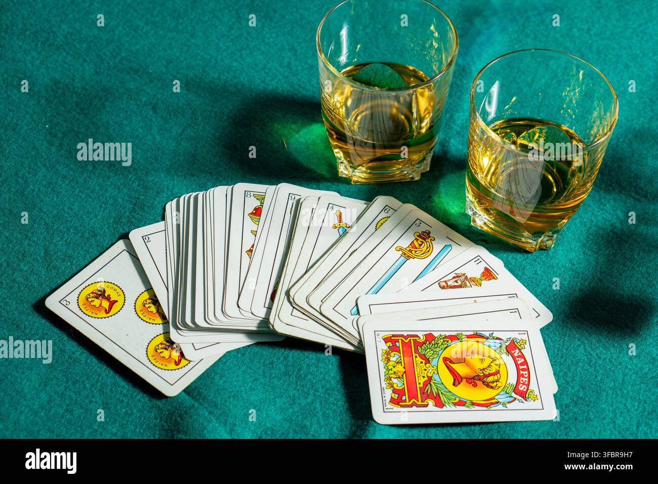 Un mazzo di carte e due bicchieri di whisky sono disposti su un tavolo verde. Le carte sono disposte in fila e gli occhiali sono riempiti con la l ambra Foto Stock