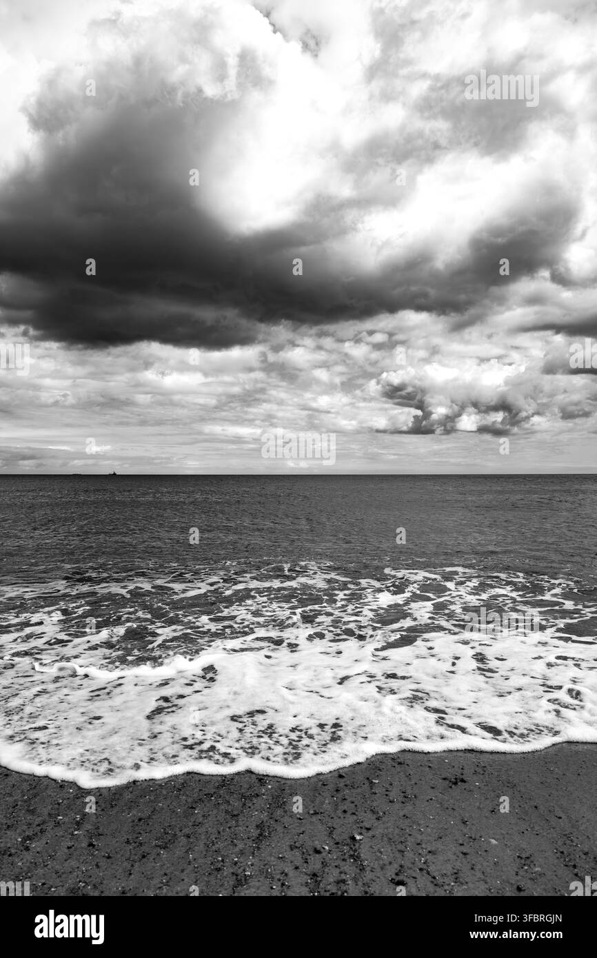 Paesaggio marino drammatico in bianco e nero con onde che si infrangono e nuvole imponenti sul Mare del Nord a Waxham Beach vicino a Horsey Gap sulla costa del Norfolk di E Foto Stock