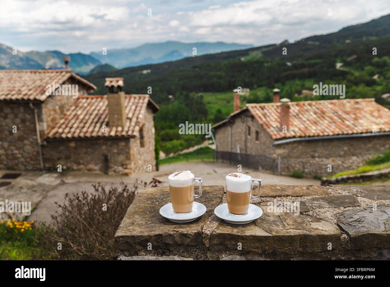 Due bevande al caffè schiumose che si affacciano su un rustico villaggio di montagna in Catalogna Foto Stock