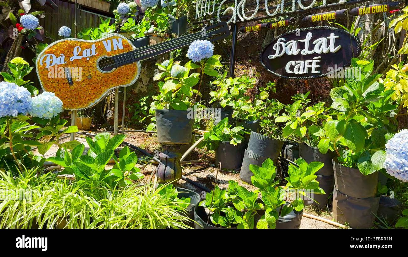 DA LAT, VIETNAM - 15 APR 2024: Un'installazione decorativa floreale a forma di chitarra circondata da ortensie blu accanto a un cartello del Da Lat Cafe a Da Lat, Vietnam. Foto Stock