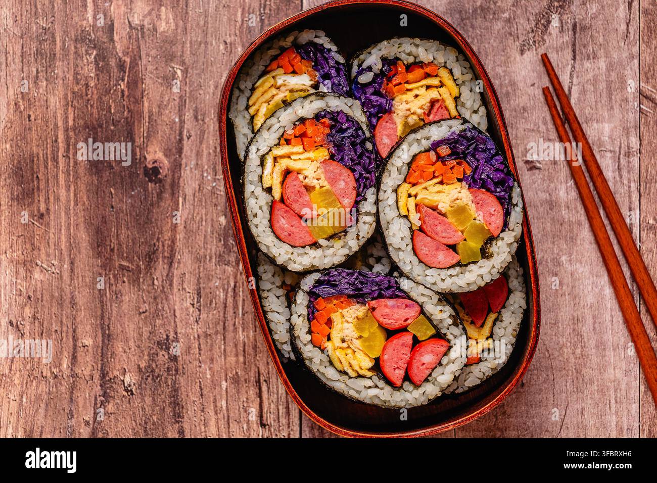 Kimbap (o gimbap) colorato con verdure e salsiccia in una scatola di legno su una superficie di legno Foto Stock
