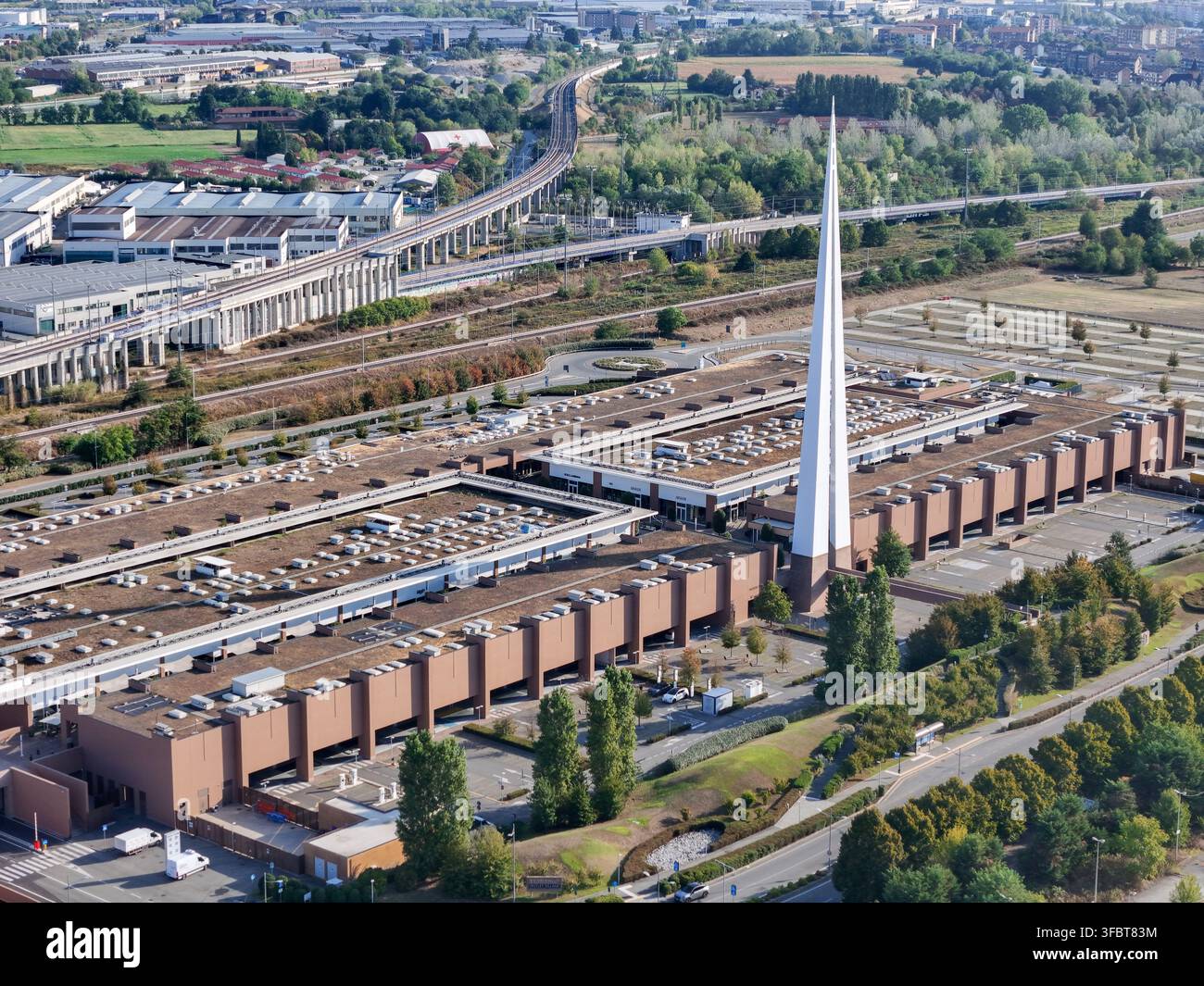 Vista aerea del Torino Outlet Village con il suo caratteristico alto campanile bianco, l'architettura moderna marrone e i parcheggi circostanti a Settimo Torinese Foto Stock