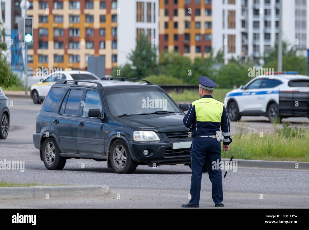 Agente del traffico ferma un SUV a un incrocio cittadino, conduce un controllo di routine sul ciglio della strada e gestisce il flusso del traffico. Foto Stock