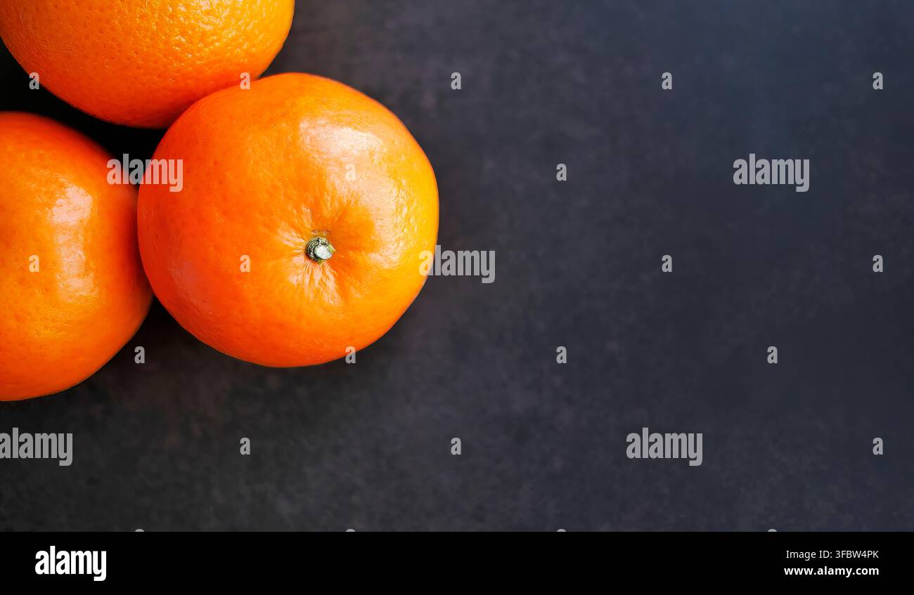 Vista ad angolo alto di mandarine biologiche mature. Frutti arancioni vibranti su texture nera. Composizione minimalista perfetta per il marketing alimentare, banner sulla salute Foto Stock
