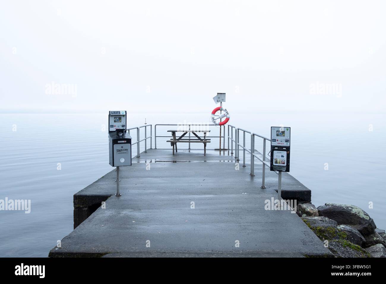 Composizione minimalista che cattura la quieta solitudine, la calma e un molo vuoto perso nella fitta nebbia mattutina. Foto Stock