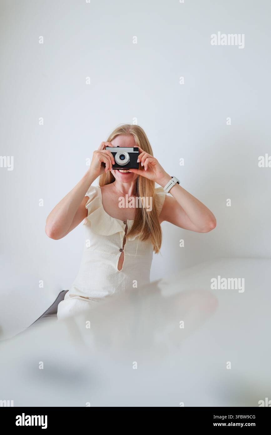 Donna allegra che tiene una fotocamera vicino al viso con un gesto della mano aperto, concetto di creazione di contenuti e fotografia. Foto Stock