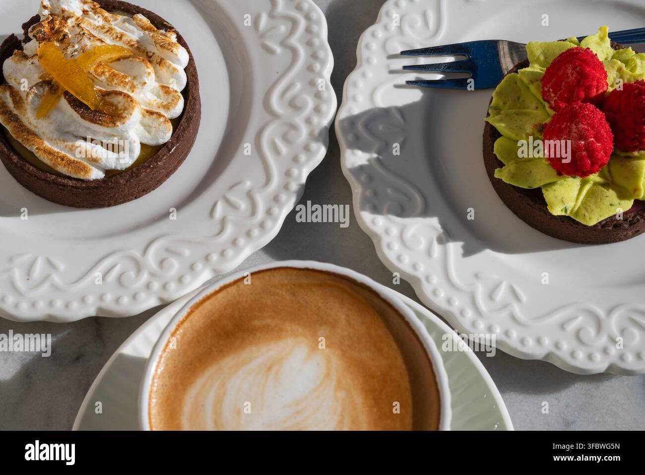 Due diverse torte gourmet servite su piatti bianchi insieme a una tazza di caffè. Foto Stock