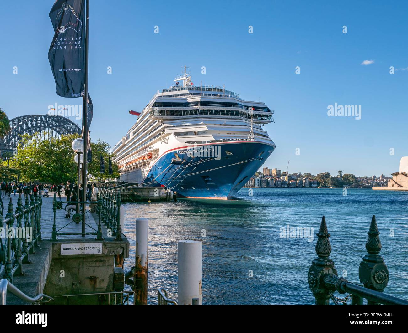 Sydney, New South Wales, Australia, 07-03-2026: Grande nave da crociera attracca vicino al porto. Cielo azzurro, acqua calma, ringhiera verde. Il ponte del porto di Sydney visibile Foto Stock