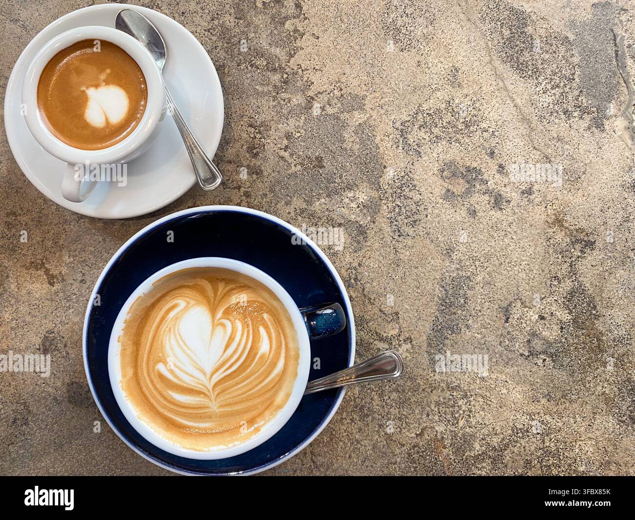 Vista piatta dall'alto di due tazze di caffè fresche con latte art posizionate sul lato di un tavolo di pietra ruvida con spazio per il testo. Foto Stock