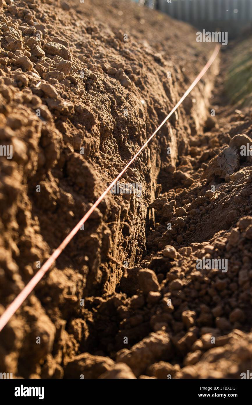 Linea di misurazione posizionata lungo una trincea di terreno appena arato in un sito agricolo. La luce naturale illumina la terra strutturata, rivelando il contenuto di umidità e la composizione delle particelle. Foto Stock
