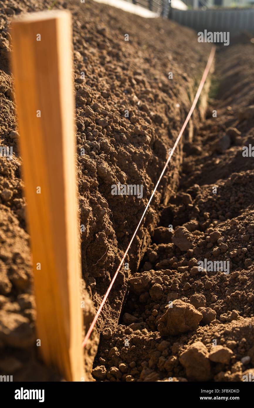 Stabilire linee guida per la semina utilizzando paletti di legno e spago in terreno preparato per il giardinaggio. Il ricco terreno marrone è organizzato in file ordinate, creando un layout strutturato per la coltivazione. Foto Stock