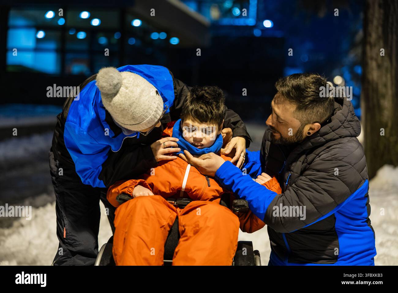 Famiglia che aiuta il figlio con bisogni speciali nella neve di notte Foto Stock
