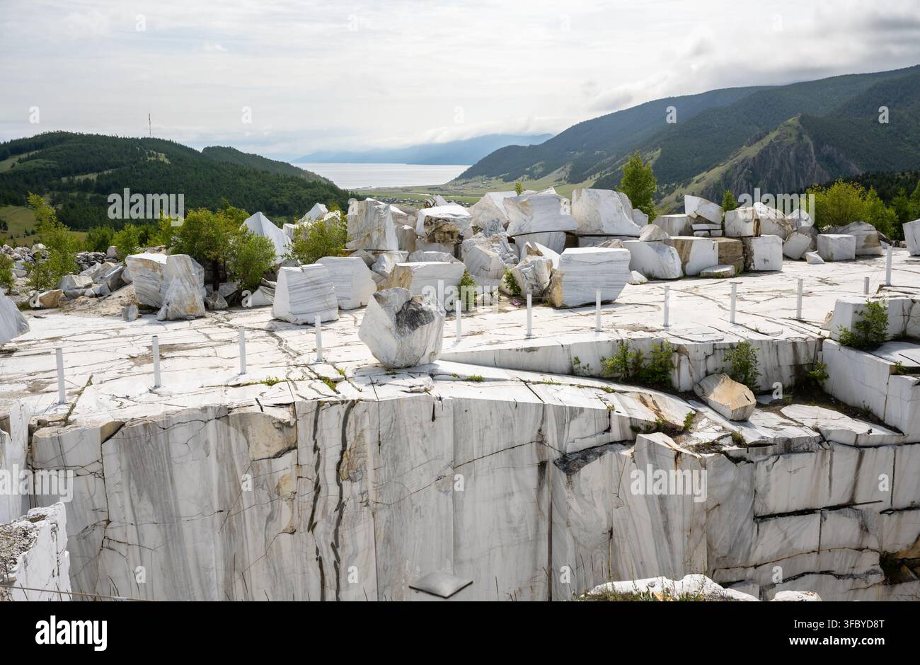 Cava di marmo bianco con grandi blocchi di pietra tagliati vicino al lago Baikal. Paesaggio di cava a cielo aperto con montagne sullo sfondo. Estrazione di risorse naturali Foto Stock