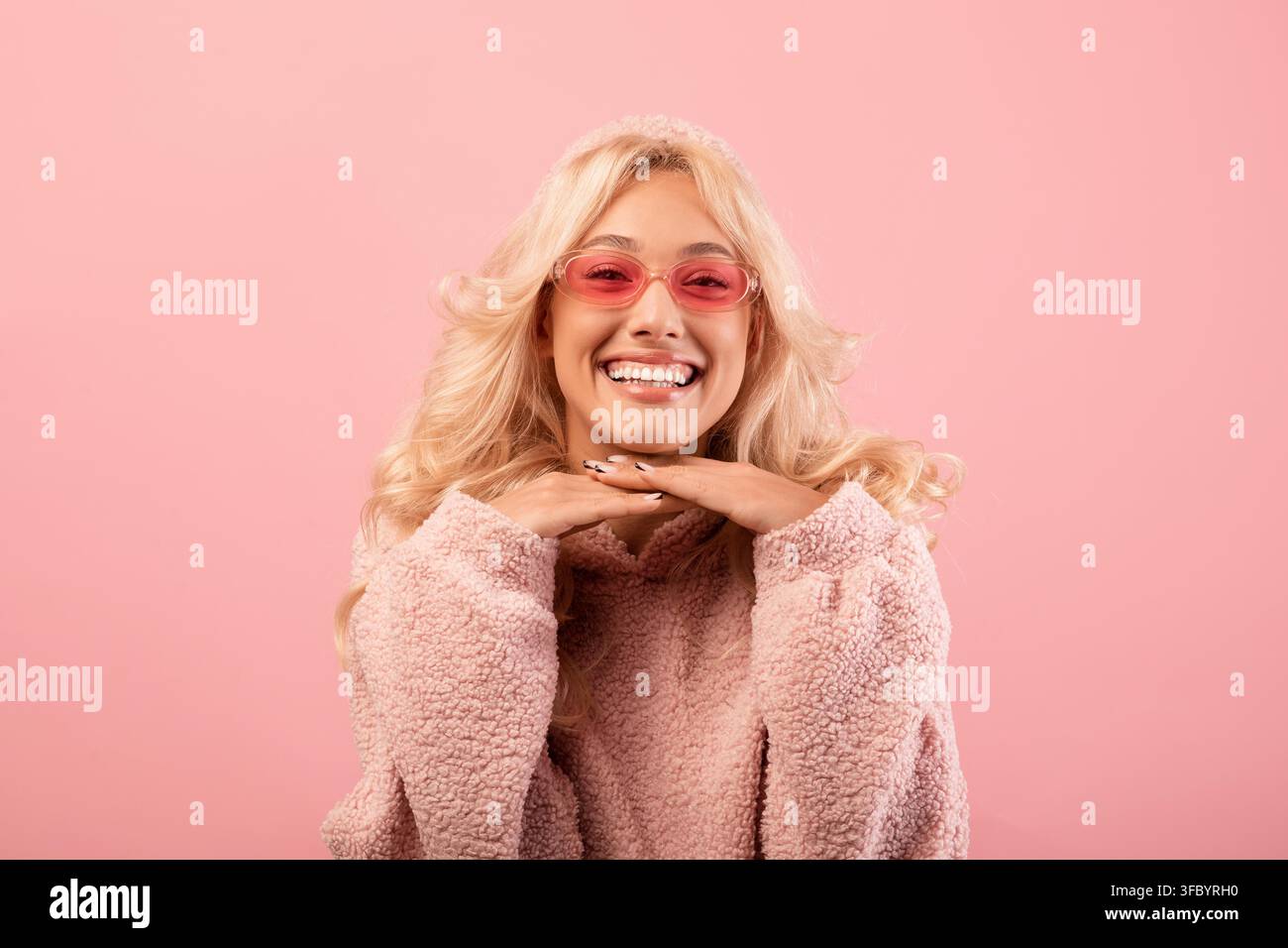 Giovane donna felice che sorride con le mani sotto il mento, sfondo rosa, concetto di bellezza Foto Stock