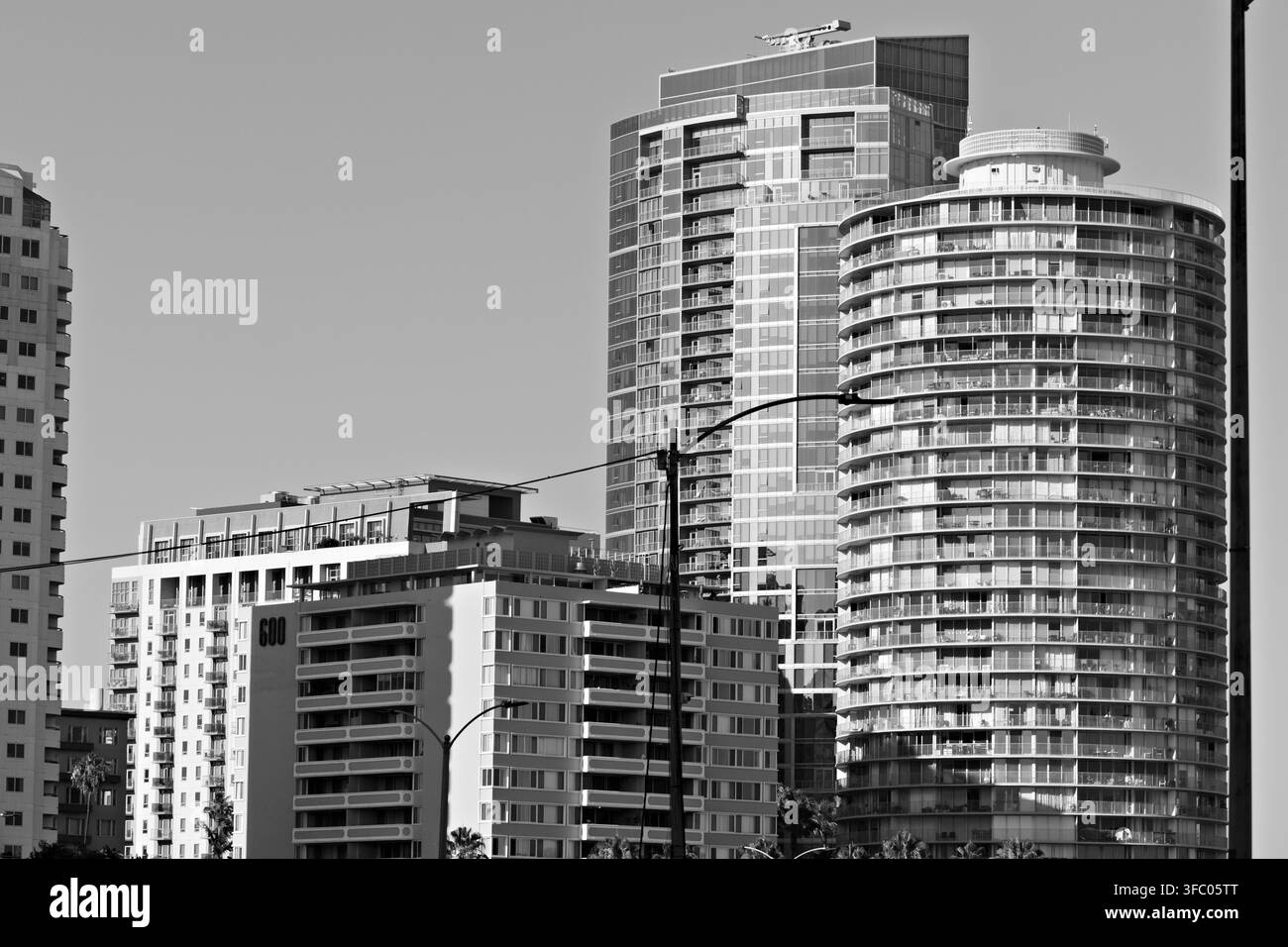 Edifici alti nel centro di Long Beach con facciate in vetro, balconi, palme e cielo azzurro limpido. Foto Stock