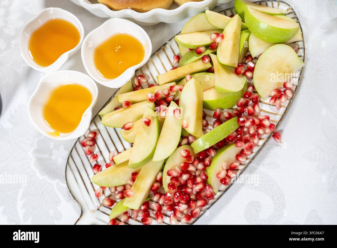 Le persone si riuniscono per Rosh Hashanah e gustano mele a fette e semi di melagrana. Il miele viene servito in piccole ciotole, aggiungendo dolcezza alla celebrazione. Foto Stock