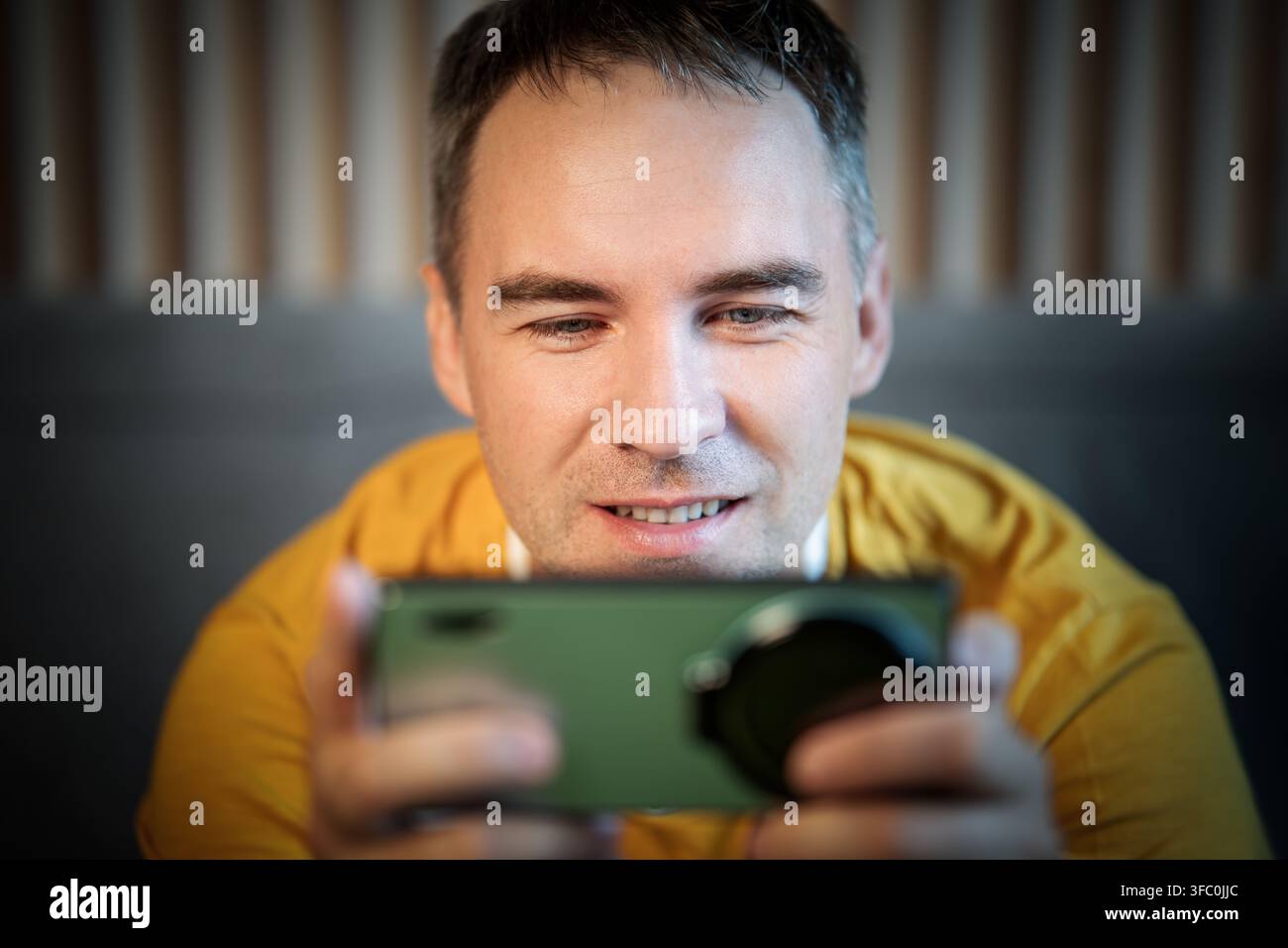 Uomo felice con gli auricolari che guarda video sullo smartphone a casa. Giovane che gioca sul telefono in primo piano Foto Stock
